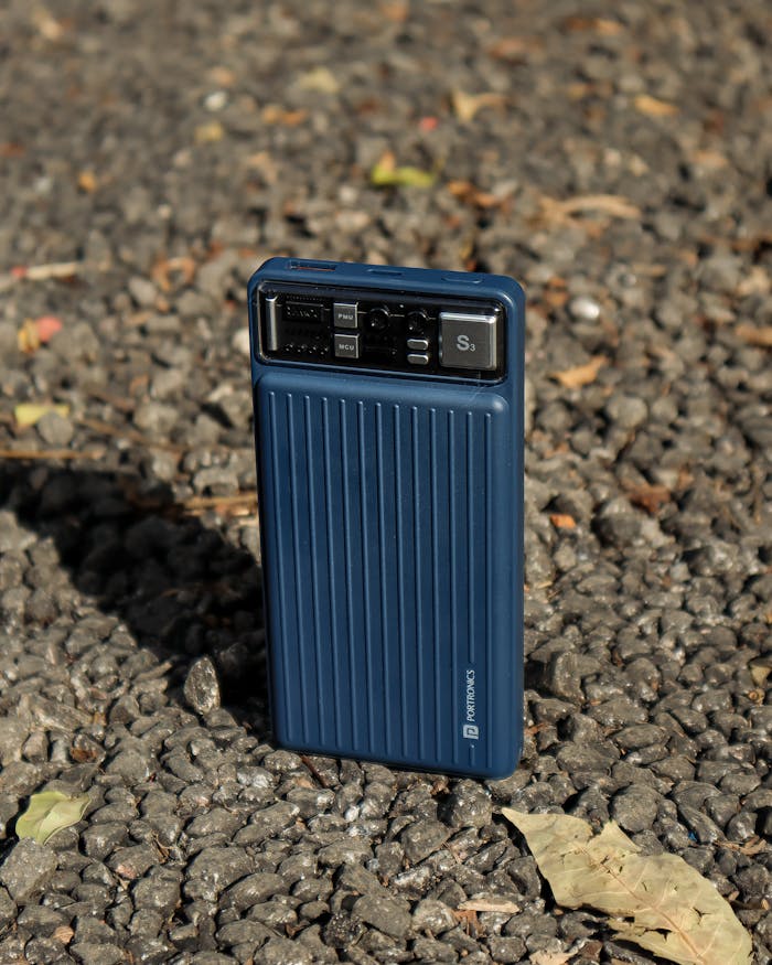 A blue power bank on a textured pebble ground, showcasing outdoor portability.